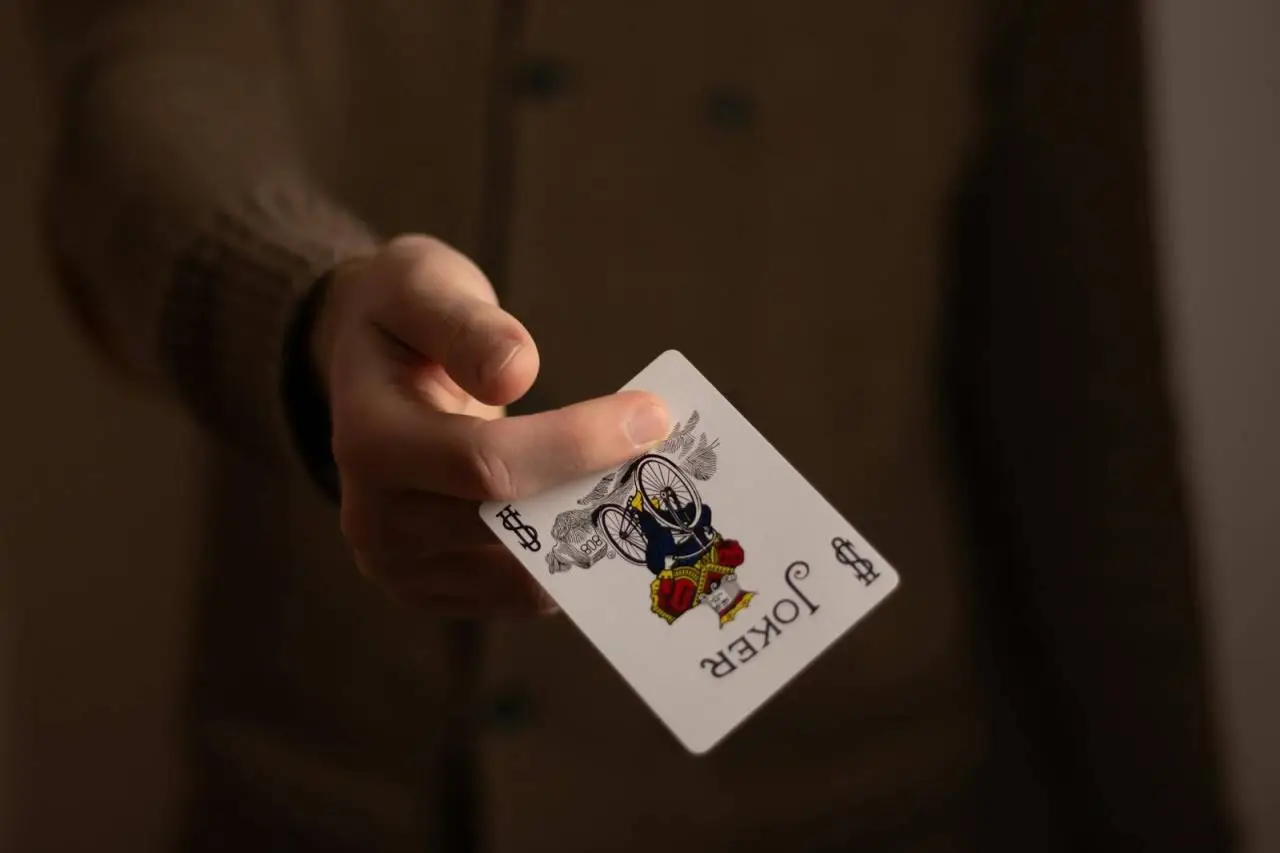 A close-up image of a hand holding a joker playing card, emphasizing gambling theme.