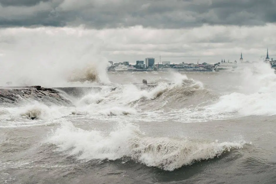 Powerful ocean waves crashing against a rocky coastline under a stormy sky with distant city skyline.