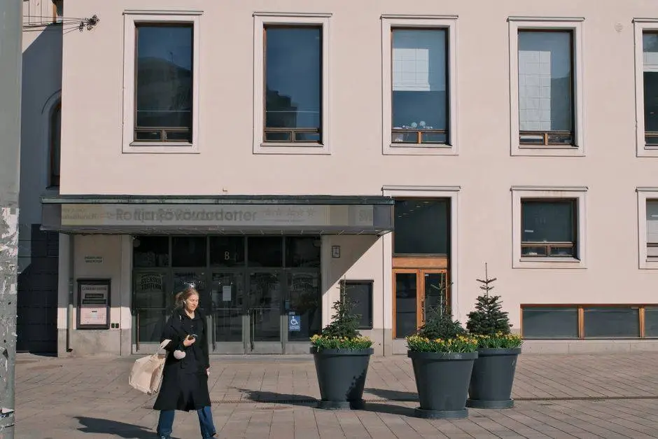 A woman walks on a sunny day outside a modern urban building with large windows.